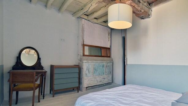 Un dormitorio con cama, cómoda, silla, espejo y lámpara colgante.