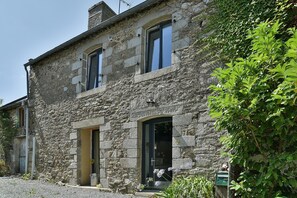 A stone building with two visible windows and a door, surrounded by greenery. - Retour aux Sources - Jolie maison familiale pour 6 (Ploubalay)