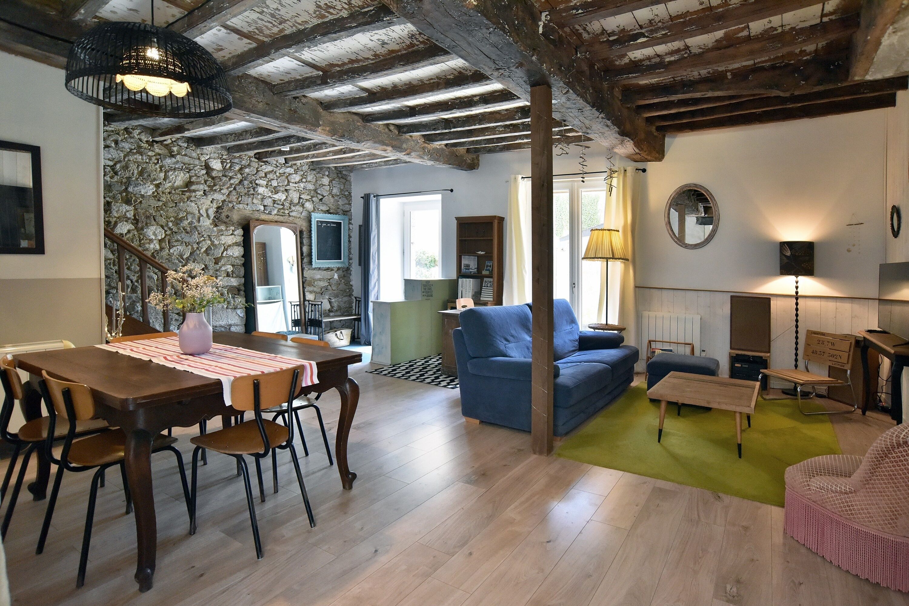 A cozy living room with a blue sofa, a dining table with chairs, and a stone wall.