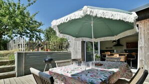 Un patio al aire libre con una mesa dispuesta para comer, rodeada de sillas de madera, bajo un gran paraguas.