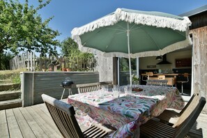 Eine Terrasse im Freien mit einem Esstisch, umgeben von Holzstühlen, unter einem großen Sonnenschirm.
