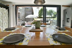 A dining table set for four with a view of a garden and outdoor seating area. - Retour aux Sources - Jolie maison familiale pour 6 (Ploubalay)