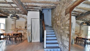 Un interior rústico con paredes de piedra vista, una escalera de madera y un comedor con mobiliario de madera.