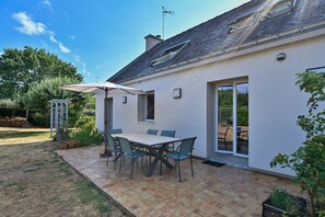 Eine Terrasse mit Tisch und Stühlen, ein überdachter Bereich und Blick auf den Garten.