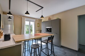 A modern kitchen with a wooden island, bar stools, pendant lighting, and a built-in oven. - Pessun - Maison pour 8 avec jardin (Berric)
