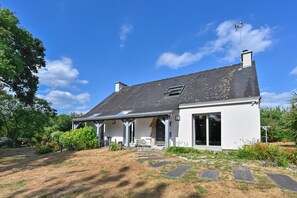 Ein zweistöckiges Haus mit geneigtem Dach, einer Veranda und einem Garten mit trittfesten Steinen, die zum Eingang führen.