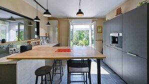 A modern kitchen with a large island, pendant lights, and a view to the outdoors. - Pessun - Maison pour 8 avec jardin (Berric)