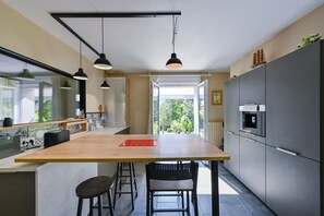 A modern kitchen with a large island, pendant lights, and a view to the outdoors. - Pessun - Maison pour 8 avec jardin (Berric)