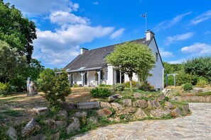 A white house with a sloped roof, a stone pathway, and a well-maintained garden with various plants and a small pond. - Pessun - Maison pour 8 avec jardin (Berric)