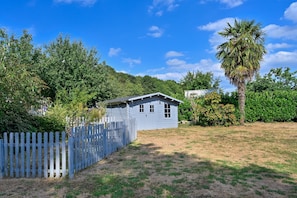 Ein eingeschossiges Haus mit umzäunter Garten, umgeben von dichter Vegetation und blauem Himmel.