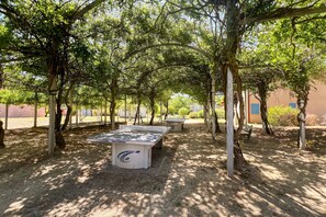 An outdoor area with a ping pong table, surrounded by trees and a building in the background. - L’Évasion Claire Rive - Proche domaines viticoles (Prayssac)