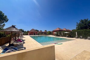 A swimming pool with lounge chairs and umbrellas, surrounded by buildings with red roofs. - L’Évasion Claire Rive - Proche domaines viticoles (Prayssac)