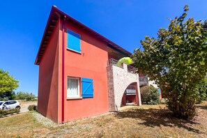 A red building with two windows, a balcony, and a stone archway. - L’Évasion Claire Rive - Proche domaines viticoles (Prayssac)