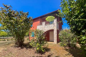 A two-story building with a stone facade, a balcony with a green umbrella, and a red roof. - L’Évasion Claire Rive - Proche domaines viticoles (Prayssac)
