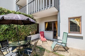 Ein Balkon mit Tisch und Stühlen, einem großen Sonnenschirm und einem Fenster mit Vorhängen.