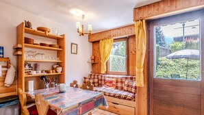 A cozy room with a wooden bench, a dining table with chairs, and a window with curtains. - Le Petit Jardin du Criou - Station de ski à 800 m (Samoëns)