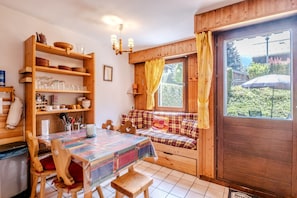 A cozy room with a wooden bench, a dining table with chairs, and a window with curtains. - Le Petit Jardin du Criou - Station de ski à 800 m (Samoëns)