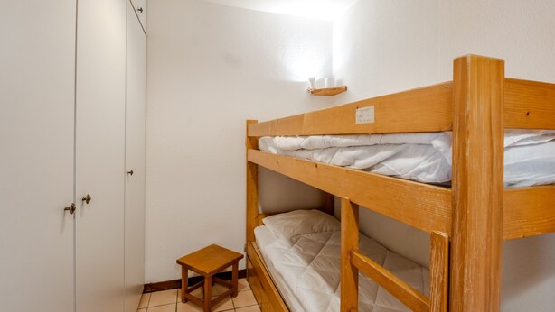A bunk bed with a wooden frame, a small wooden stool, and a white wall with a light switch. - Le Petit Jardin du Criou - Station de ski à 800 m (Samoëns)
