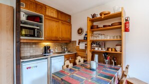 A compact kitchen with wooden cabinets, a microwave, a Bosch dishwasher, and a table with a colorful tablecloth. - Le Petit Jardin du Criou - Station de ski à 800 m (Samoëns)