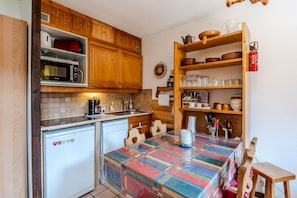A compact kitchen with wooden cabinets, a microwave, a Bosch dishwasher, and a table with a colorful tablecloth. - Le Petit Jardin du Criou - Station de ski à 800 m (Samoëns)