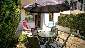 An outdoor patio with a round table and chairs, a red chair, and a large umbrella providing shade. - Le Petit Jardin du Criou - Station de ski à 800 m (Samoëns)