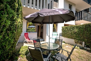 An outdoor patio with a round table and chairs, a red chair, and a large umbrella providing shade. - Le Petit Jardin du Criou - Station de ski à 800 m (Samoëns)