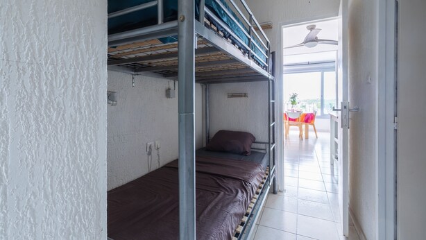 A dormitory room with bunk beds, a small table with chairs, and a view of the outdoors through a door. - Le Flamant Rose - Climatisé et à 200 m de la plage (Mauguio)