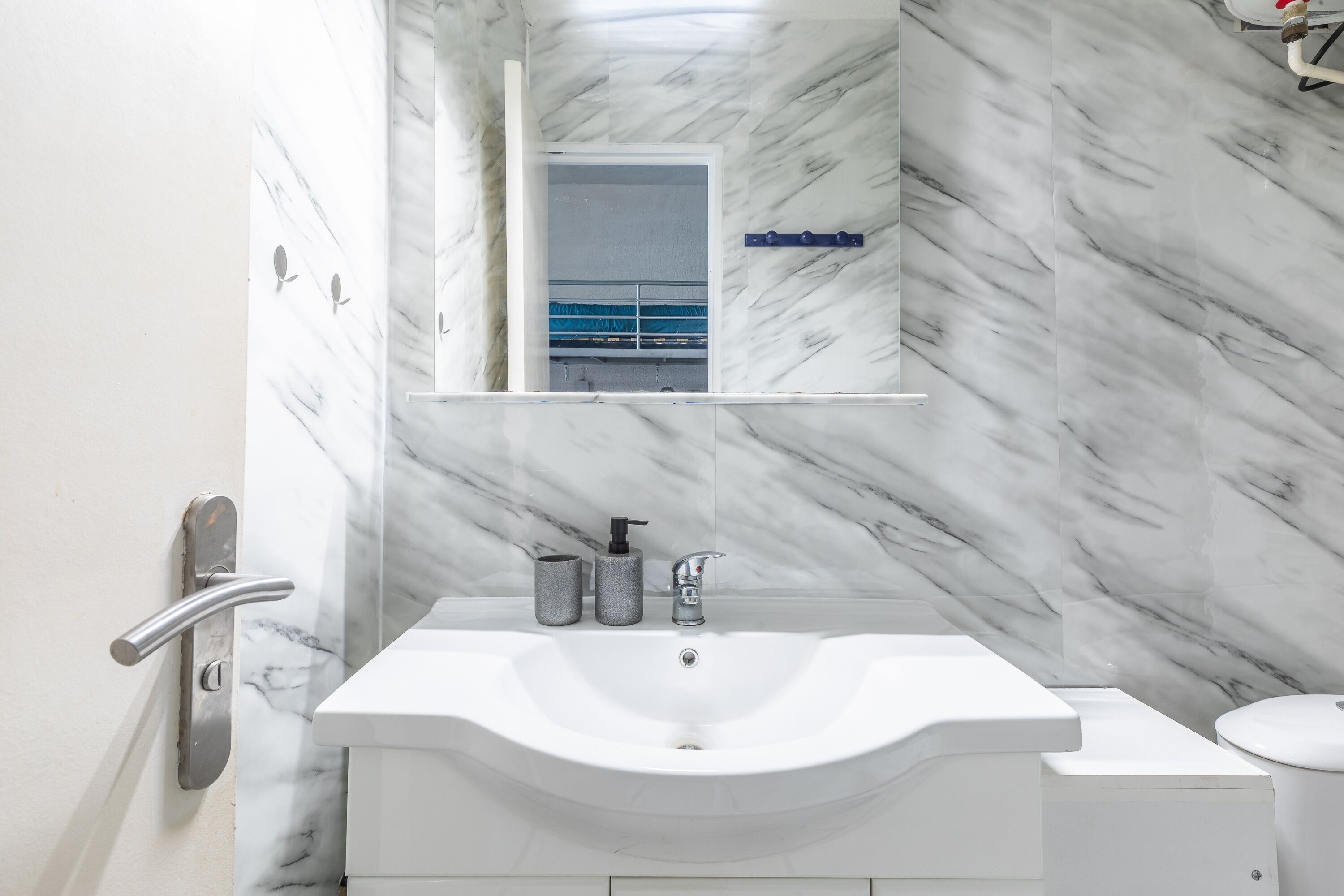 A bathroom with a white sink, a mirror, and a marble wall.