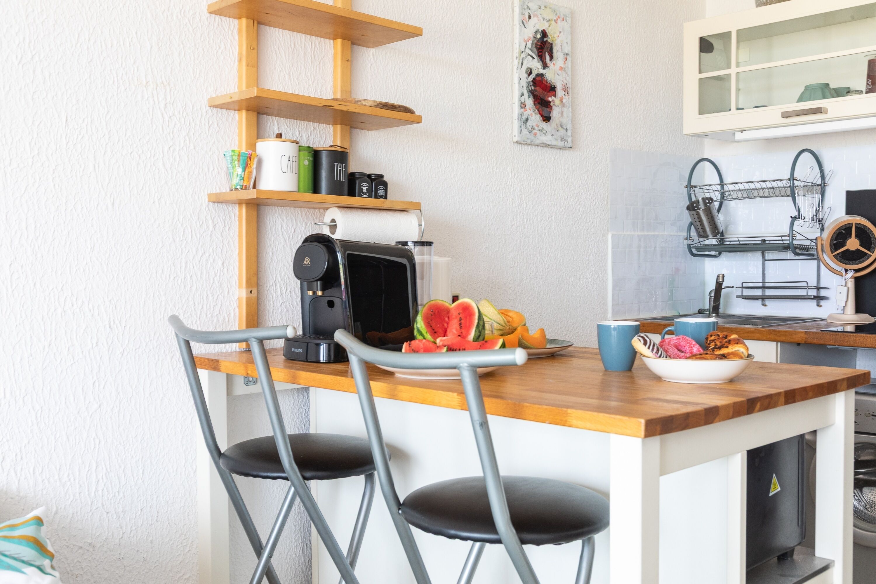 Cocina compacta con encimera de madera, cafetera, frutero y microondas.