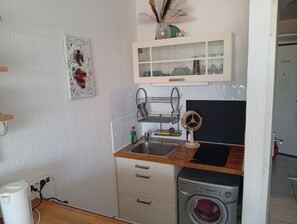 Une petite cuisine équipée d’un lave-linge, d’un évier et d’un meuble de rangement au-dessus.