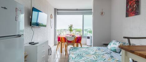 Habitación de hotel pequeña con cama, escritorio, mesa de comedor y balcón con vistas.