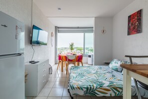 Kompakti hotellihuone, jossa on sänky, työpöytä, ruokapöytä ja parveke, jolta on näkymä.