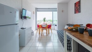 A modern kitchen with a built-in fridge, a flat-screen TV, and a dining area with a table and chairs. - Le Flamant Rose - Climatisé et à 200 m de la plage (Mauguio)