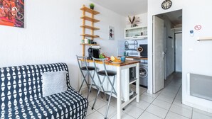 A compact living space with a kitchenette, a dining area, and a seating area with a patterned sofa. - Le Flamant Rose - Climatisé et à 200 m de la plage (Mauguio)