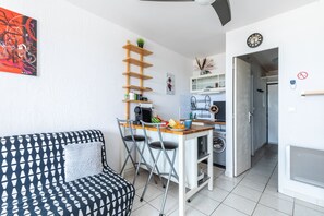 A compact living space with a kitchenette, a dining area, and a seating area with a patterned sofa. - Le Flamant Rose - Climatisé et à 200 m de la plage (Mauguio)
