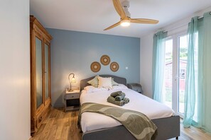 Ein Schlafzimmer mit einem Bett, Nachttischen, einem Deckenventilator und einem Fenster mit Vorhängen.