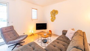 A modern living room with a grey sofa, a patterned armchair, a small wooden coffee table, and a flat-screen TV mounted on the wall. - L’Horizon de Ribérac - Piscine privée chauffée (Saint-Martin-de-Ribérac)