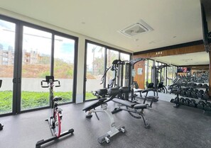 Un gimnasio con equipo de ejercicio, ventanas amplias y vistas a edificios.