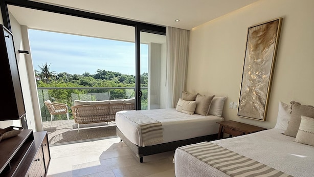 A modern hotel room with a balcony, a large bed, a bedside table, and a television. - Loft 10 minutes from the beach, 2 queen-size beds, kitchenette, Wi-Fi, gym, Nuevo Vallarta (Flamingos)