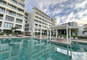 Ein modernes Hotel mit Schwimmbad, mehreren Balkonen und einer überdachten Außenbereich-Sitzgelegenheit.