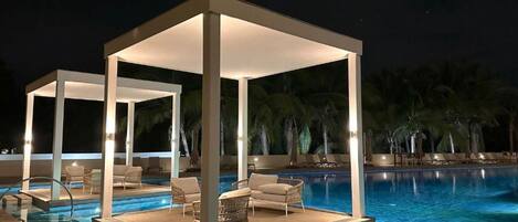 Zona junto a la piscina con un área de estar cubierta, sillas de descanso y una piscina.