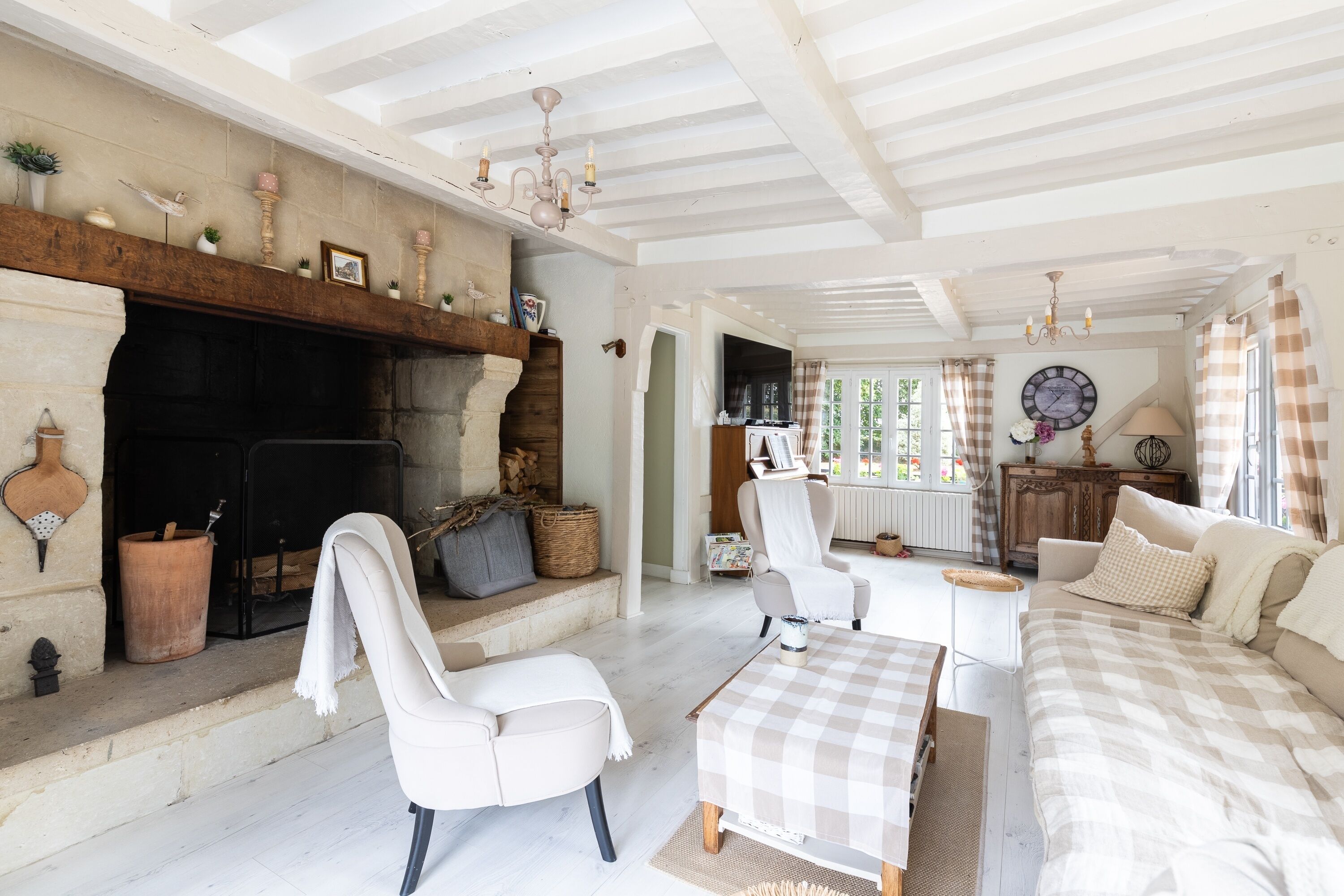 Una sala acogedora con chimenea, un sofá cómodo, un sillón blanco y una mesa a cuadros.