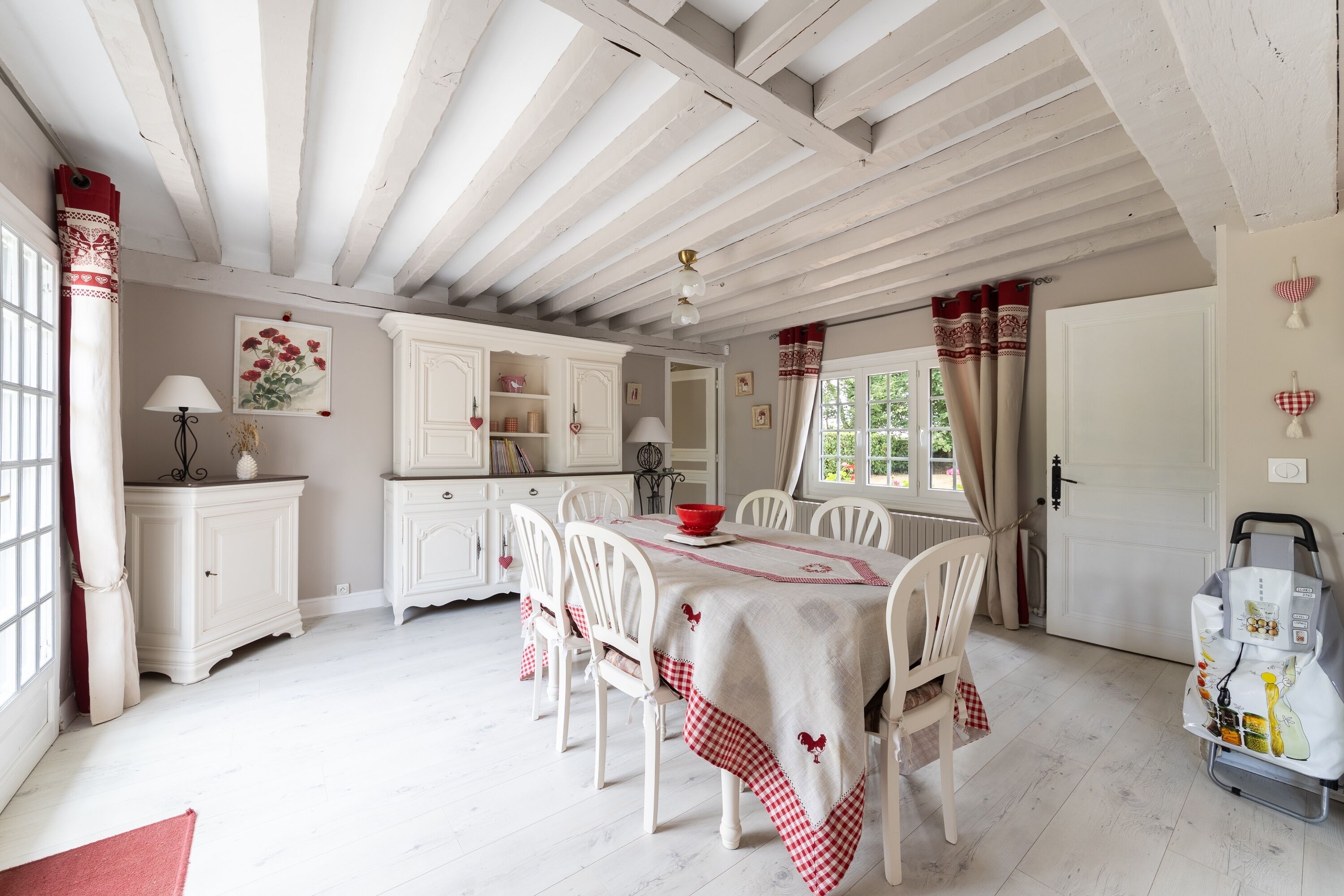 Un comedor con una mesa dispuesta para cuatro, sillas blancas y mantel a cuadros rojo y blanco.