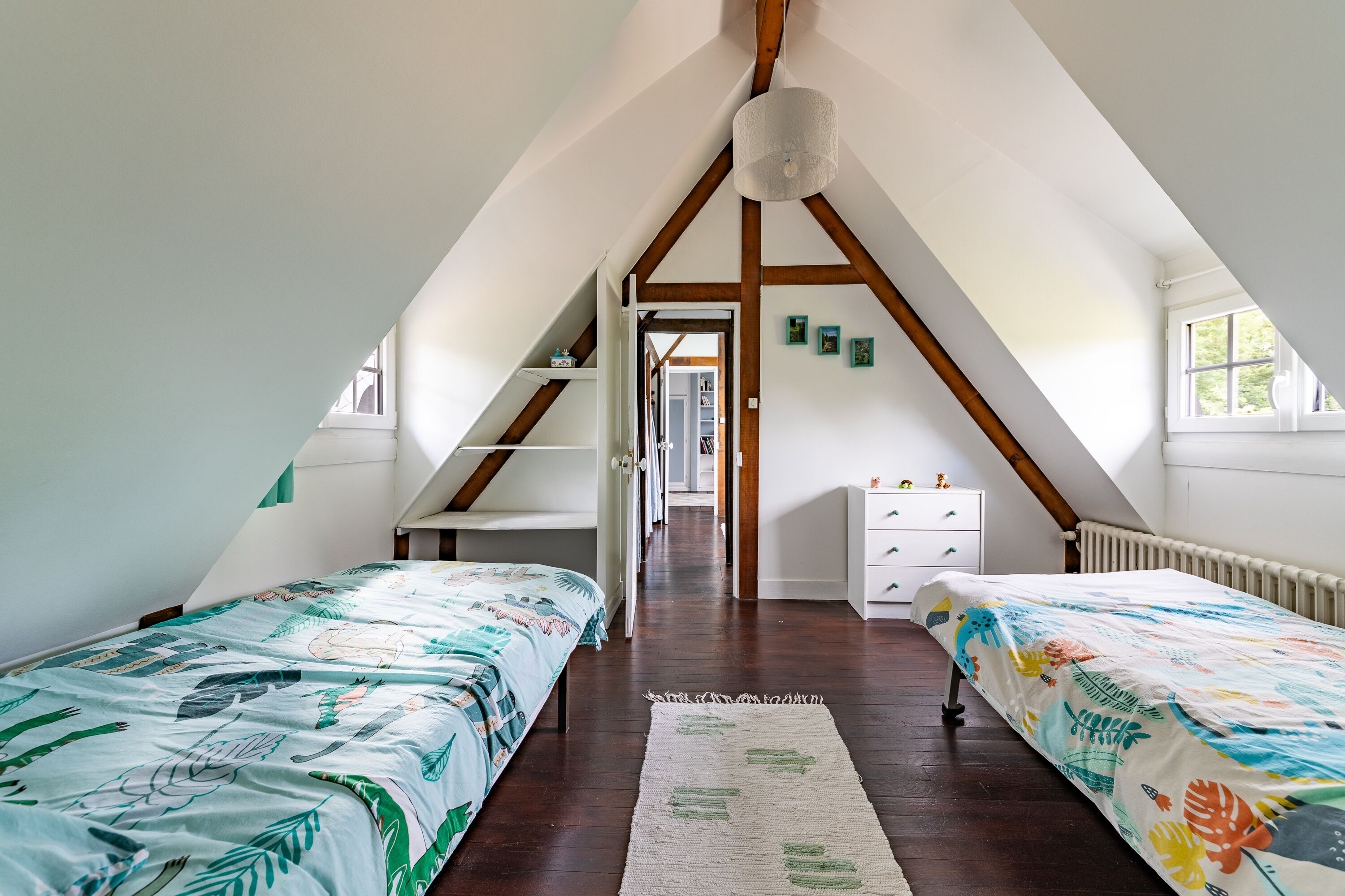 A bedroom with two beds, a white dresser, and a wooden ceiling structure.