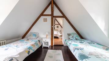 A bedroom with two single beds, a white nightstand with a lamp, and a wooden ceiling structure.