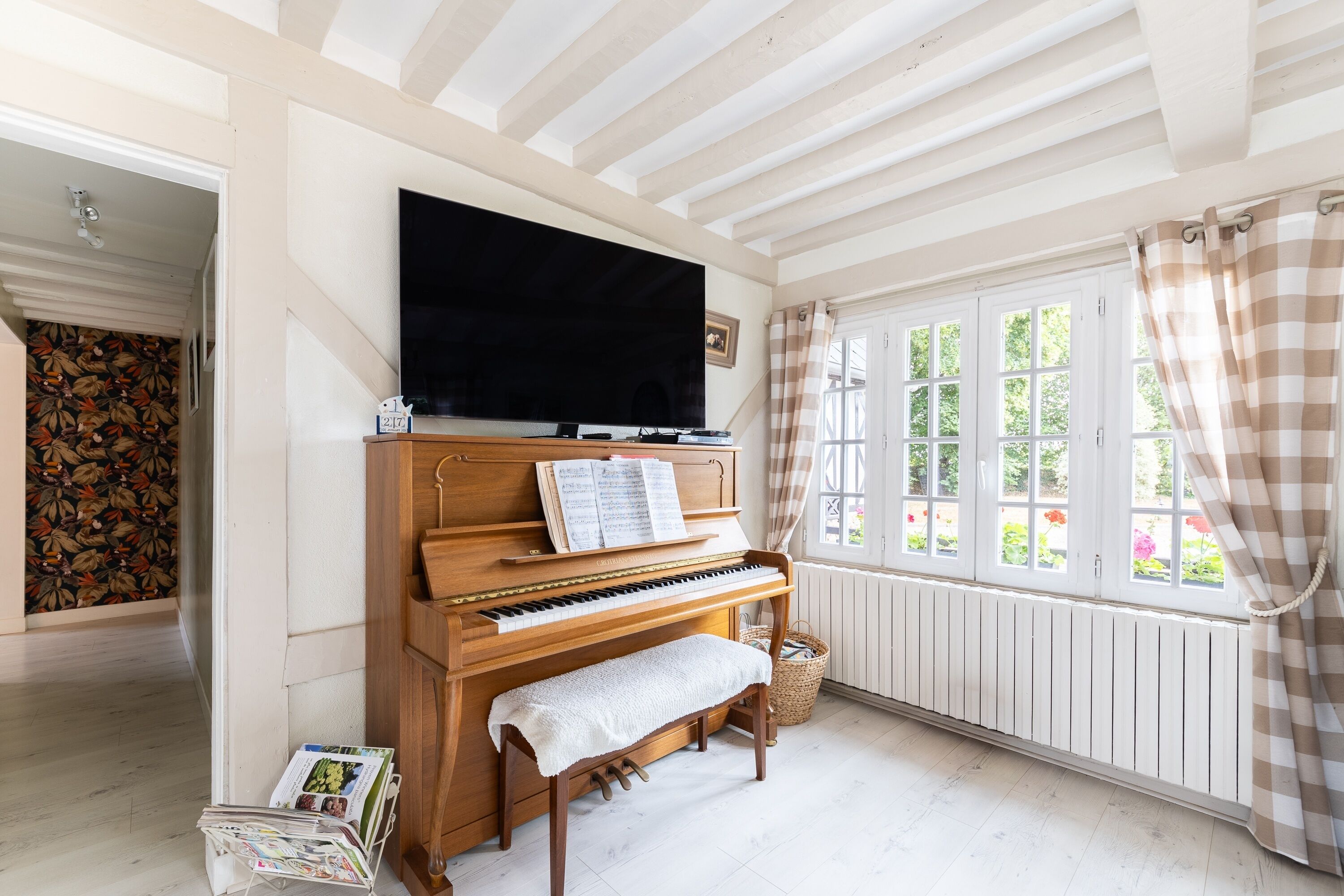 A piano with sheet music, a television above it, and a window with curtains.