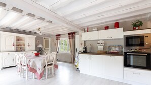 A kitchen with white cabinetry, a dining table with chairs, and a microwave oven. - La Maison Maudanaur - Maison familiale avec jardin (Morainville-Jouveaux)