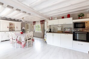 A kitchen with white cabinetry, a dining table with chairs, and a microwave oven. - La Maison Maudanaur - Maison familiale avec jardin (Morainville-Jouveaux)
