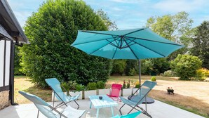 An outdoor patio with a table and four chairs, a large umbrella, and a well-maintained garden. - La Maison Maudanaur - Maison familiale avec jardin (Morainville-Jouveaux)