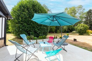 An outdoor patio with a table and four chairs, a large umbrella, and a well-maintained garden. - La Maison Maudanaur - Maison familiale avec jardin (Morainville-Jouveaux)